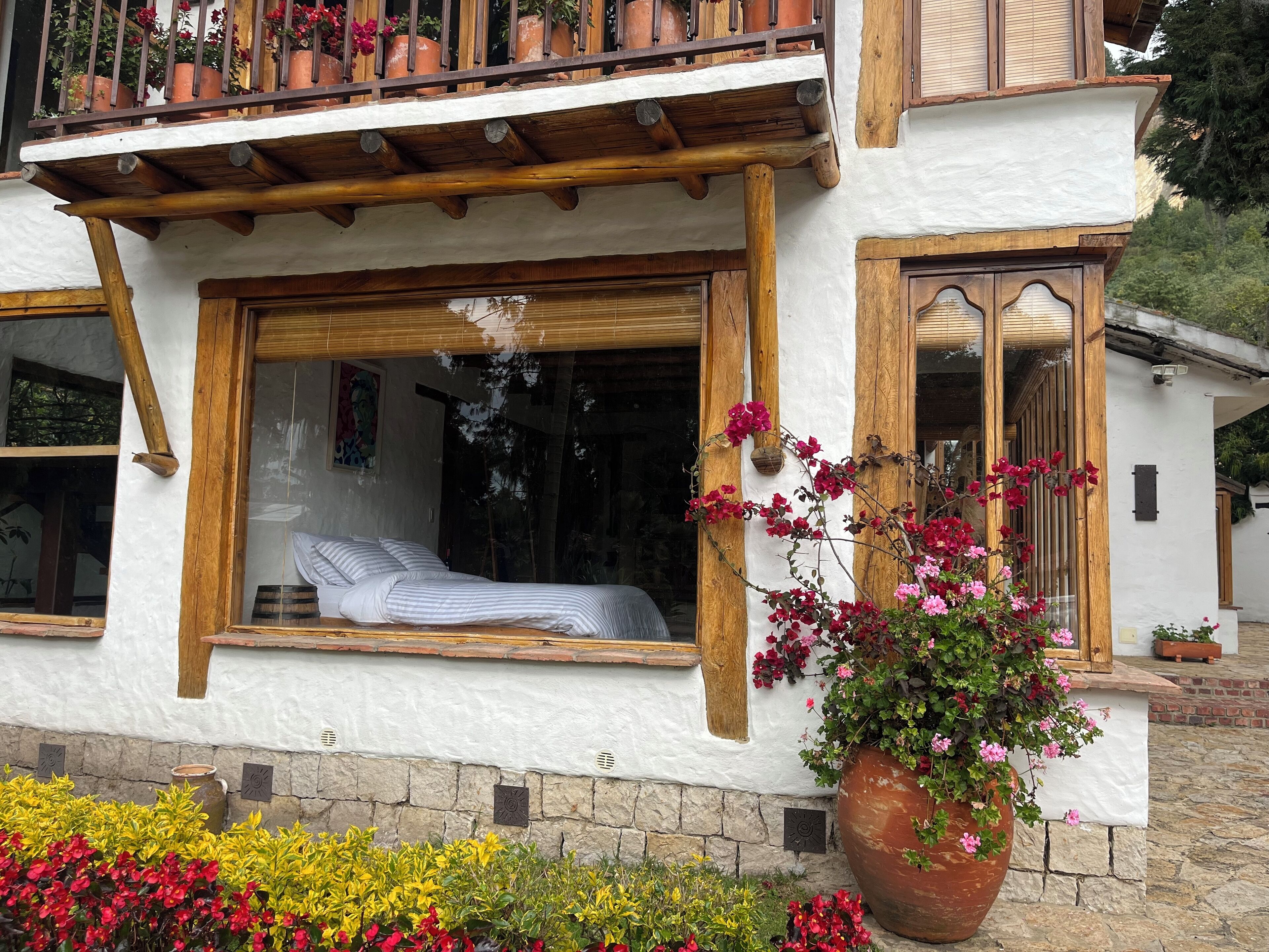 A traditional chalet with a wooden balcony, large windows, and a stone foundation.