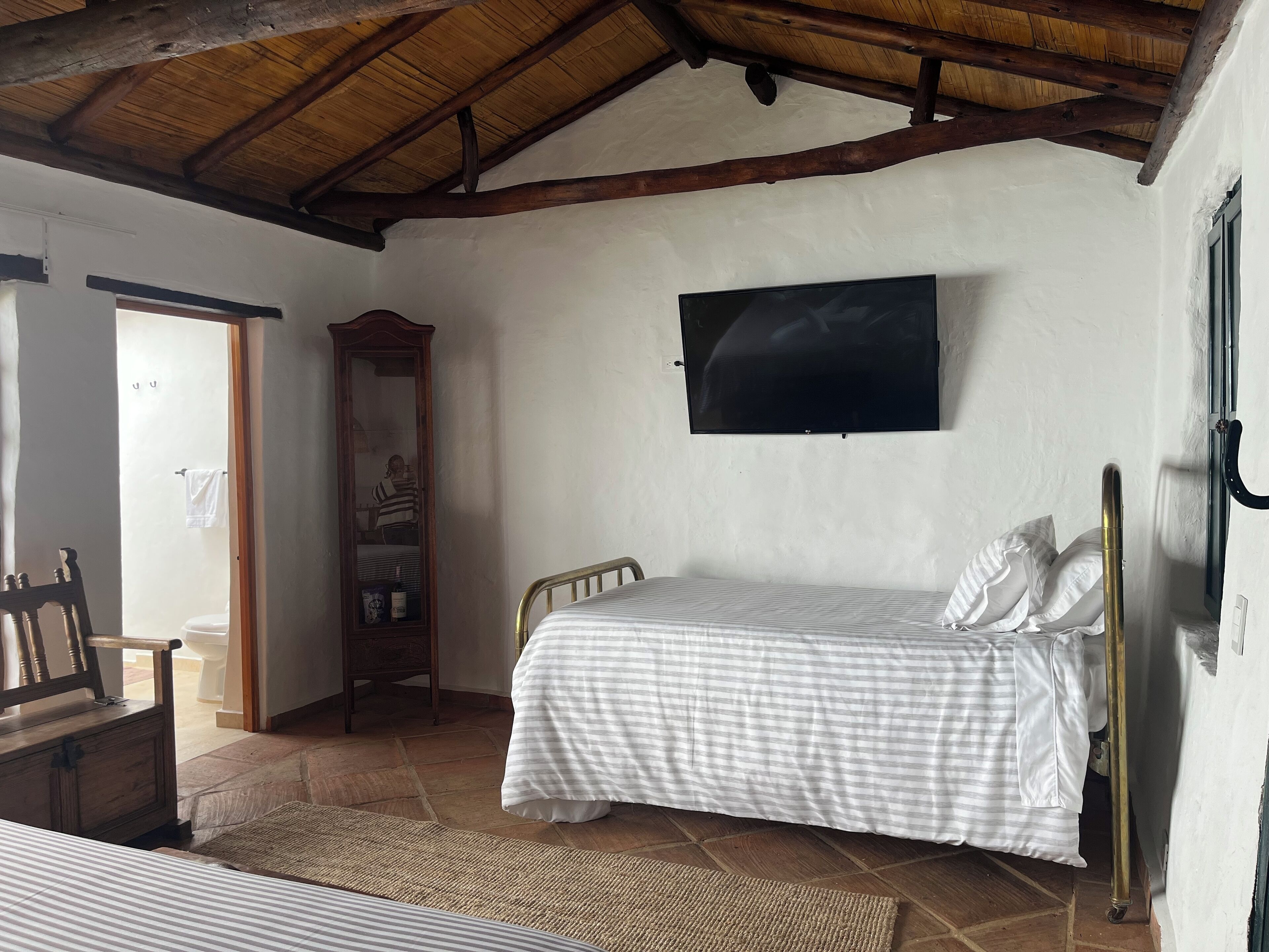 A bedroom with two beds, a television, a wooden wardrobe, and a mirror.