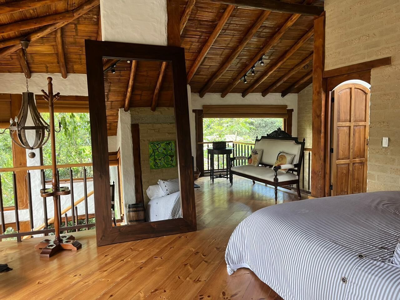 A wooden-floored room with a bed, a mirror, and a view of an outdoor patio with a sofa and a table.