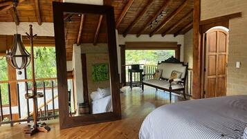 A wooden-floored room with a bed, a mirror, and a view of an outdoor patio with a sofa and a table.