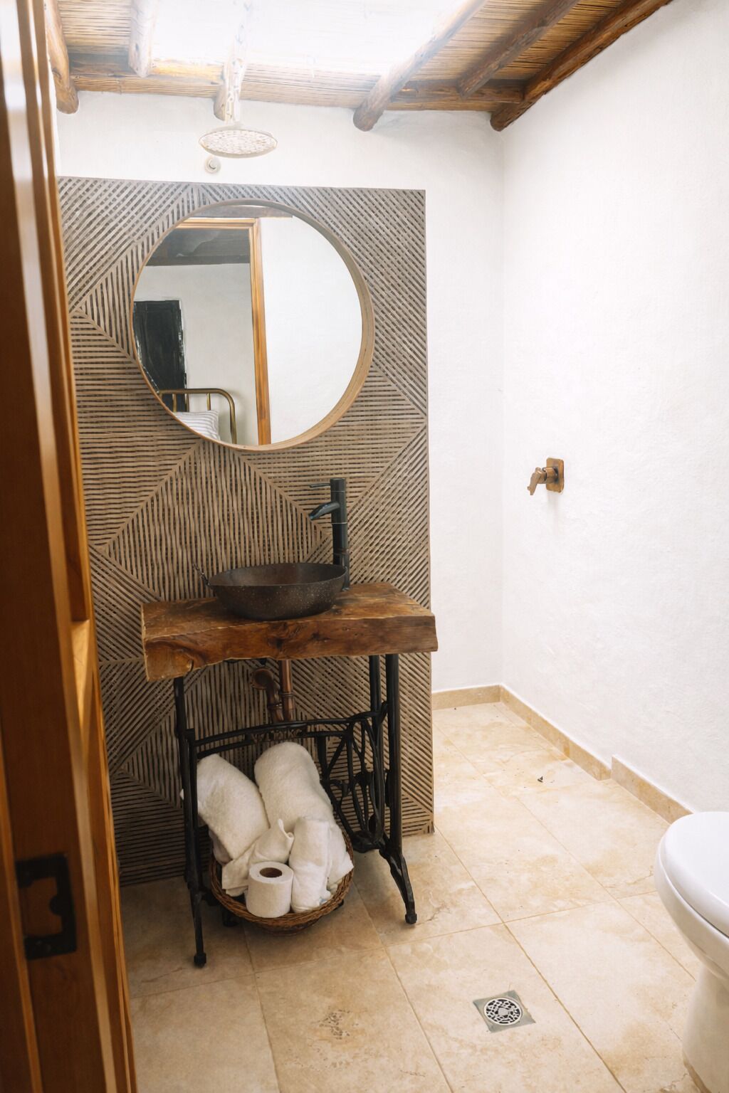 A bathroom with a round mirror, wooden sink, and a metal stool with towels.