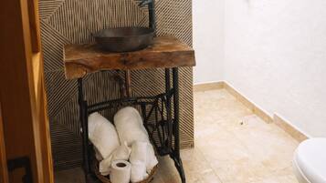 A bathroom with a round mirror, wooden sink, and a metal stool with towels.