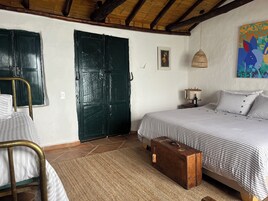 Un dormitorio con una cama, una puerta verde, una lámpara de mimbre y un cuadro colorido.