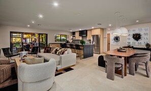 Eine moderne Küche mit einer zentralen Kochinsel, ein Essbereich mit Holztisch und Stühlen sowie ein Wohnzimmer mit Sofas und einem Couchtisch.
