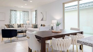 Una sala de estar moderna con comedor, que presenta una gran mesa de madera, sillas blancas tapizadas y un conjunto de sofá.