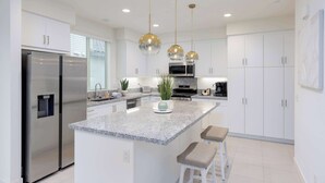 Una cocina moderna con armarios blancos, electrodomésticos de acero inoxidable, una isla de granito e iluminación colgante.
