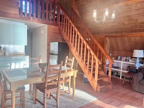 A wooden interior with a dining table, chairs, a kitchen area, and a staircase. - Hawberry Haven - Waterfront, Private Sandy Beach on Mudge Bay, Kagawong (Kagawong)