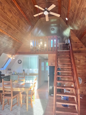 A wooden interior with a dining area, kitchen, and a staircase leading to an upper level. - Hawberry Haven - Waterfront, Private Sandy Beach on Mudge Bay, Kagawong (Kagawong)