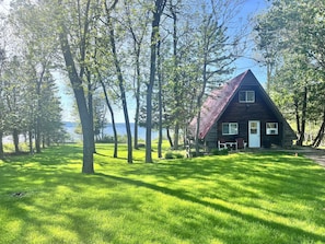 A cabin with a sloped roof, surrounded by trees and a grassy area. - Hawberry Haven - Waterfront, Private Sandy Beach on Mudge Bay, Kagawong (Kagawong)