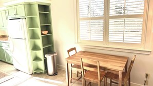 Een keuken met een groen kastje, een houten tafel en een raam met jaloezieën.