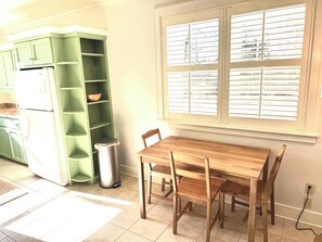 Une cuisine avec un meuble vert, une table en bois et une fenêtre avec des stores.