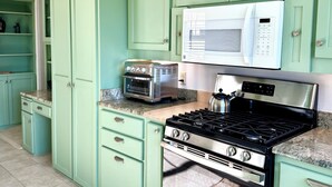 Een keuken met blauwgroene kastjes, een magnetron, een broodrooster en een fornuis.
