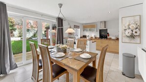 Une cuisine moderne avec des meubles en bois, un coin repas doté d’une table en verre et une vue sur un jardin grâce à de grandes portes coulissantes.