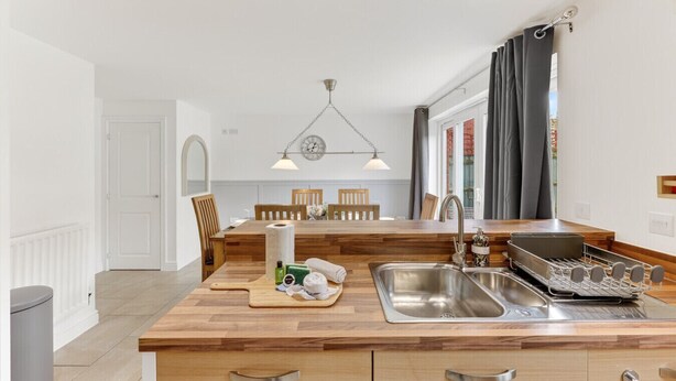 Une cuisine moderne avec des meubles en bois, un évier en acier inoxydable et un îlot central en bois doté d’une planche à découper et d’ustensiles de cuisine essentiels.