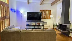 A living room with a sofa, a flat-screen TV, a fireplace, and a wall-mounted shelf with decorative items. - Golf and Campus Getaway  EV, Near Hospitals- 3 Bedroom, 2.5 Bath (Memphis)