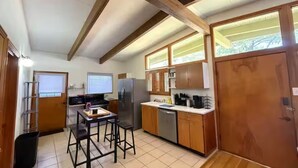 A compact kitchen with wooden cabinets, a stainless steel refrigerator, and a small dining area with stools. - Golf and Campus Getaway  EV, Near Hospitals- 3 Bedroom, 2.5 Bath (Memphis)