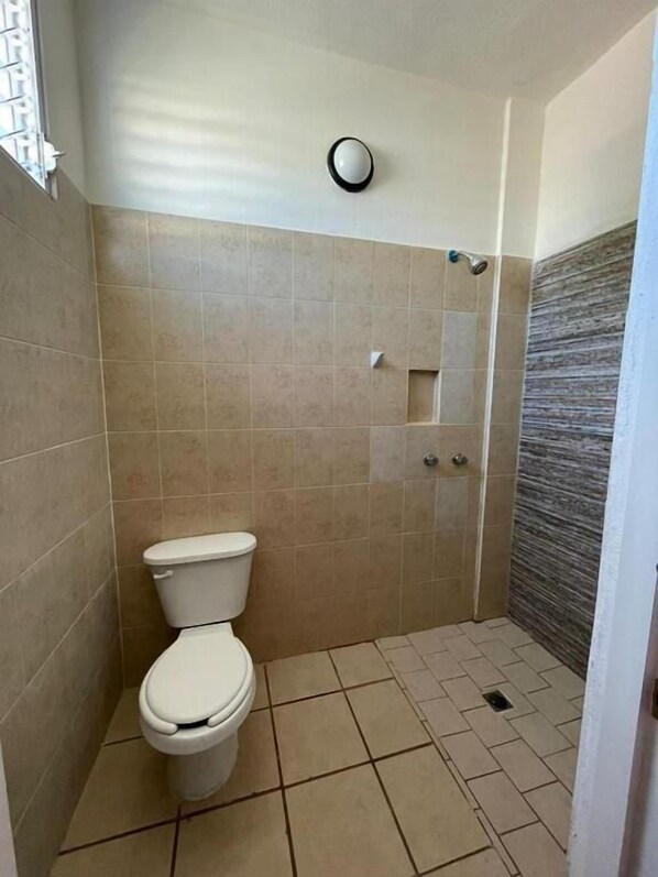 Ein kleines Badezimmer mit Fliesen, einer Toilette, einer Dusche und einem Handtuchhalter an der Wand.