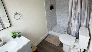 Une salle de bain moderne avec un meuble-lavabo blanc, des toilettes, une douche avec un mur en marbre et un luminaire au plafond.