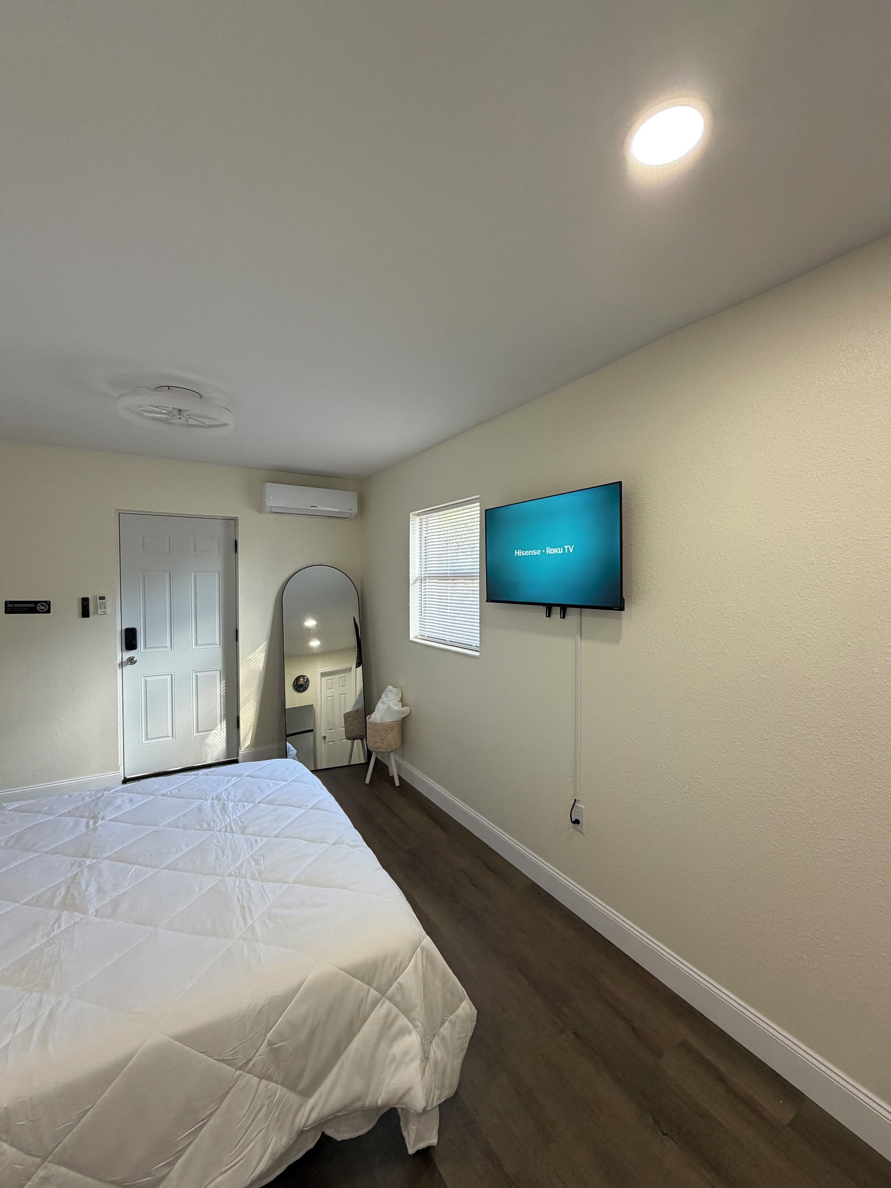 A hotel room with a bed, a TV mounted on the wall, a door, and an air conditioning unit.