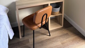 Une chambre à coucher comprenant un lit, un bureau en bois, une chaise et une œuvre d’art accrochée au mur.