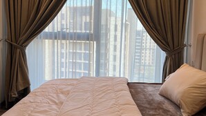 A hotel room with a large bed, a smaller bed, a window with curtains, and a view of buildings outside.