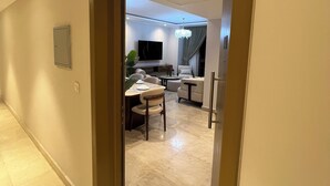 A hallway leading to a living area with a dining table, chairs, a sofa, and a TV.