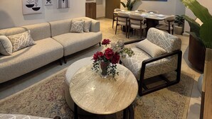 A modern living room with a sectional sofa, a round coffee table, a dining area with a table and chairs, and a large potted plant.