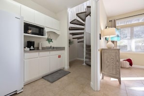 A kitchen with white cabinets, a microwave, and a staircase leading to another level. - Walk to Beach,  Gameroom, Golden Hour Getaway, Laguna Beach (Panama City Beach)