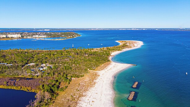 Et luftfoto af et kystområde med en strand, klart blåt vand og et skovområde.