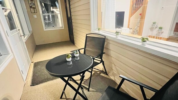 Een klein terras met een ronde tafel en twee stoelen, een raam met uitzicht op een trap, en een deur die naar een andere kamer leidt.