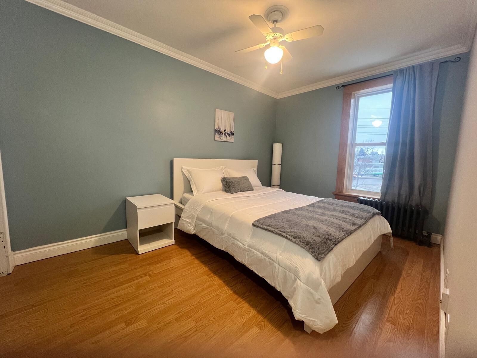 Une chambre à coucher avec un lit, une table de chevet, un ventilateur de plafond et une fenêtre avec des rideaux.