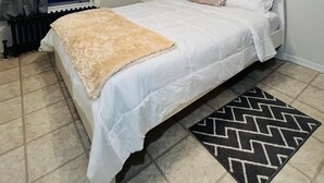 Een slaapkamer met een bed, een plafondventilator, een raam met gordijnen, een radiator en een vloerkleed.