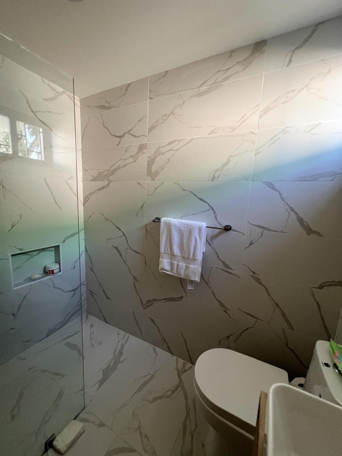 A bathroom with marble walls, a glass shower enclosure, a toilet, and a towel rack.