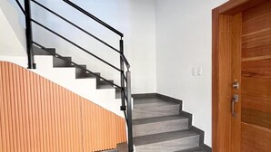A modern staircase with a wooden handrail and grey steps, leading to a wooden door. - Quiet and cozy place (Santo Domingo)