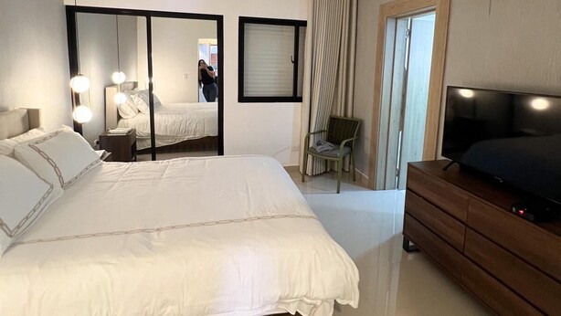 A modern hotel room with a large bed, a TV, a dresser, a chair, and a mirror. - Quiet and cozy place (Santo Domingo)