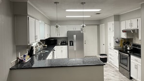 Una cucina moderna con mobili bianchi, un piano di lavoro nero, elettrodomestici in acciaio inossidabile e illuminazione a sospensione.