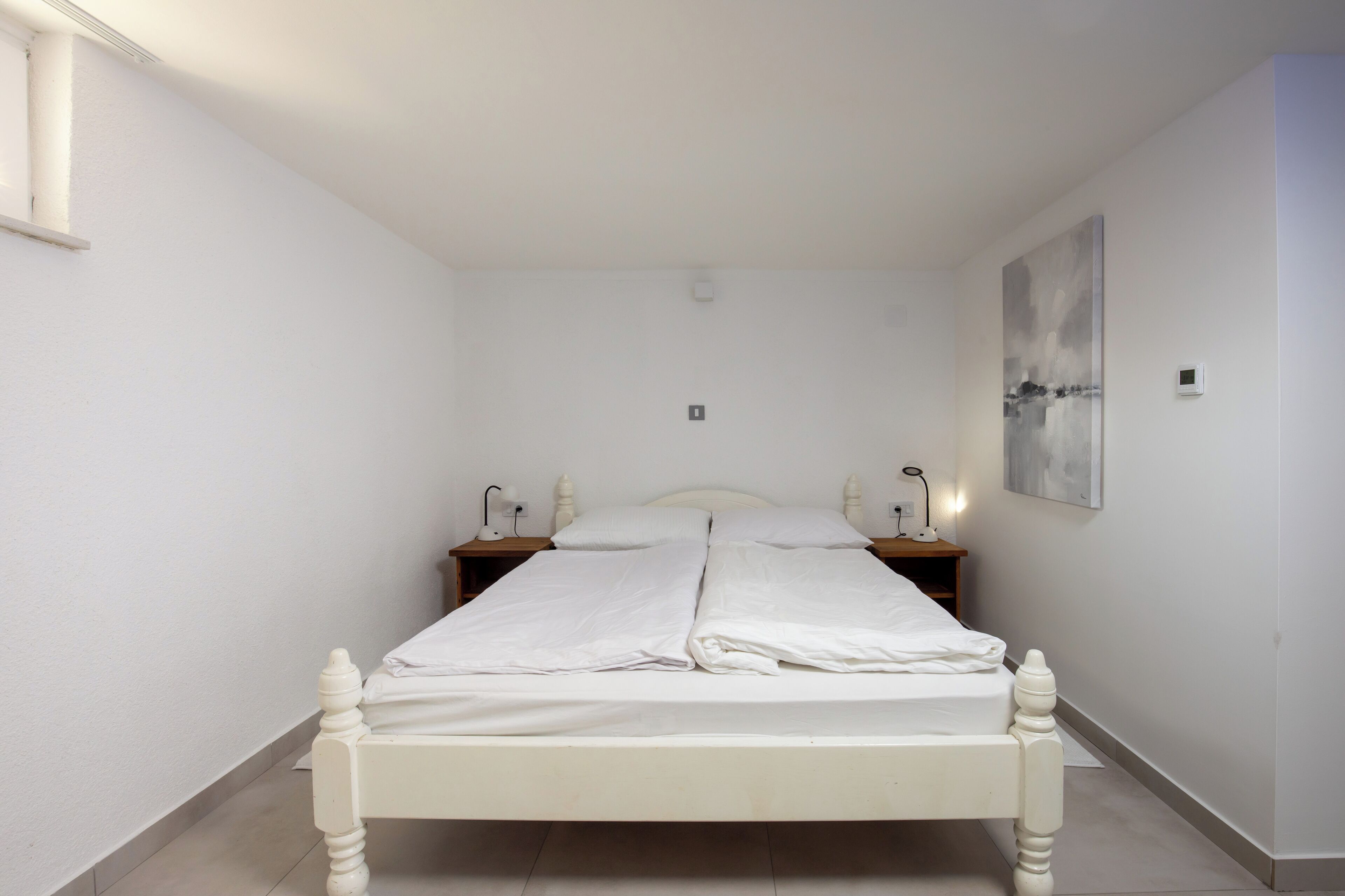 Una cama con dosel blanco, con un cabecero de madera, dos mesitas de noche con lámparas y un aplique de pared.