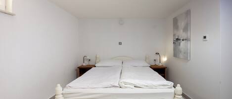 Una cama con dosel blanco, con un cabecero de madera, dos mesitas de noche con lámparas y un aplique de pared.
