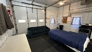 Habitació petita amb literes, sofà, cuina americana i finestra amb cortines.