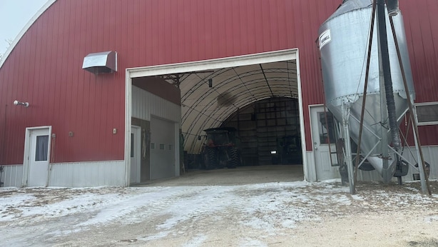 Un edifici industrial gran amb façana vermella i una porta gran oberta. A l'interior, hi ha un gran siló metàl·lic i un tractor.