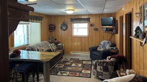 L’intérieur chaleureux d’un chalet, avec un décor en bois, un téléviseur fixé au mur, une table à manger avec des bancs et une cheminée.