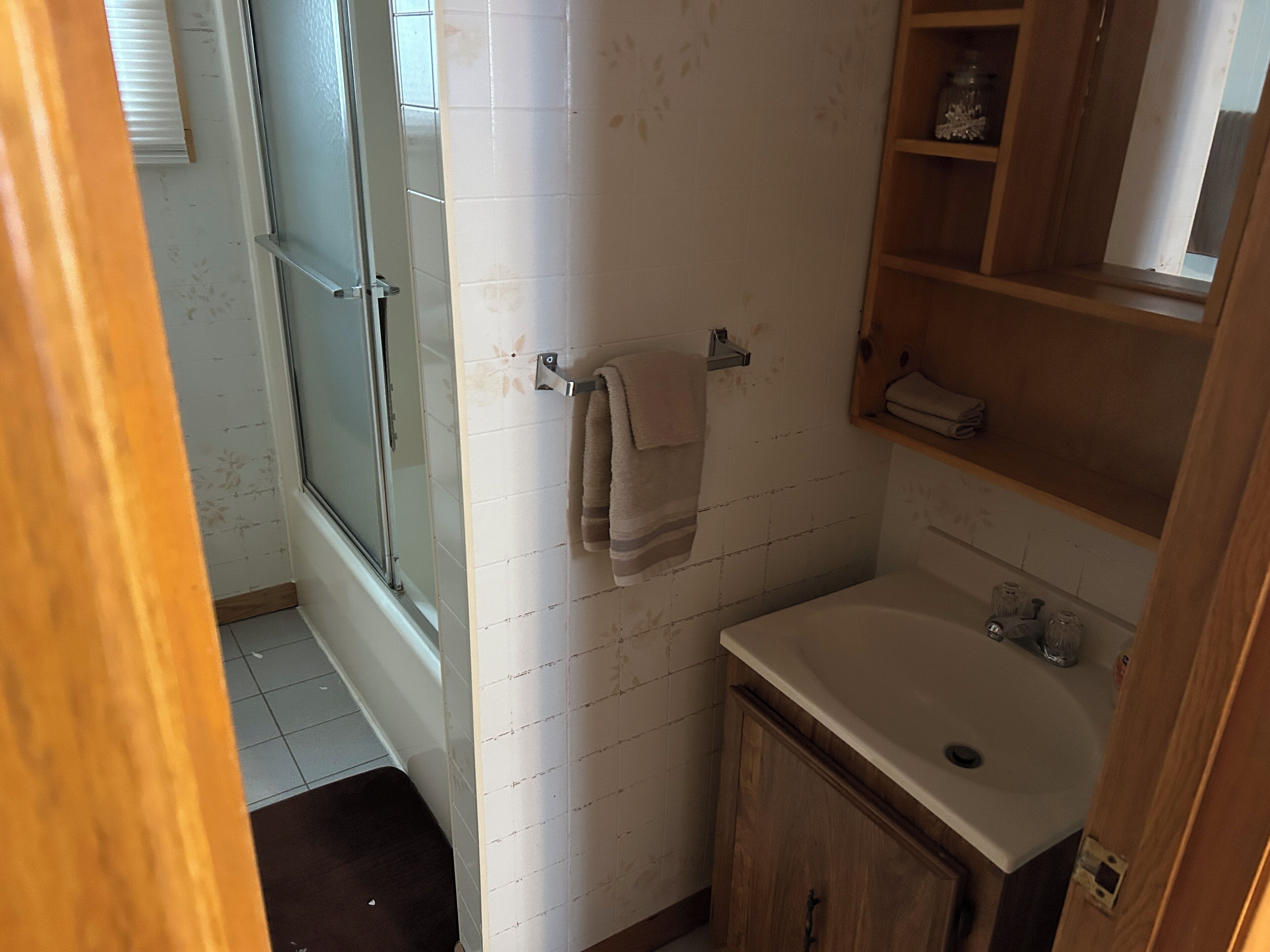Une salle de bain avec une porte de douche en verre, un lavabo et des étagères en bois.