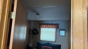 Une chambre à coucher avec un lit, une fenêtre avec des stores, un ventilateur de plafond et une couronne décorative accrochée au mur.