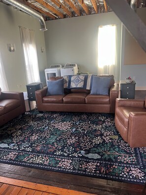 A cozy living room with a brown leather sofa, a patterned rug, and a washing machine in the background.