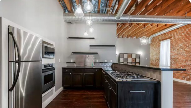 A modern kitchen with stainless steel appliances, dark cabinetry, and a brick accent wall. - Historic Luxury on Main Street in Spring Hill (Spring Hill)