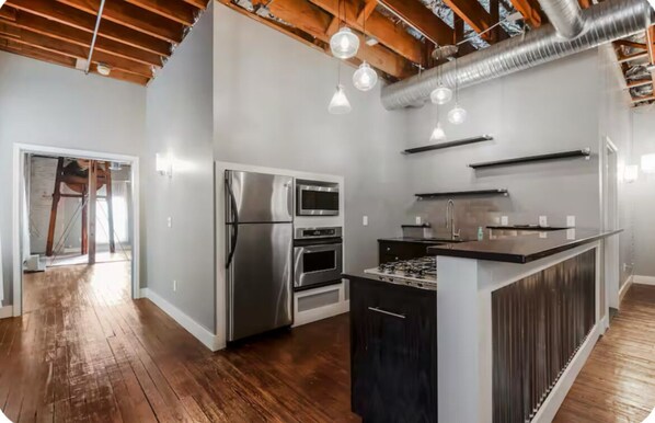 A modern kitchen with stainless steel appliances, wooden flooring, and pendant lighting.