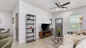 Ein Wohnzimmer mit Sofa, Fernseher, Regalen und Deckenventilator.
