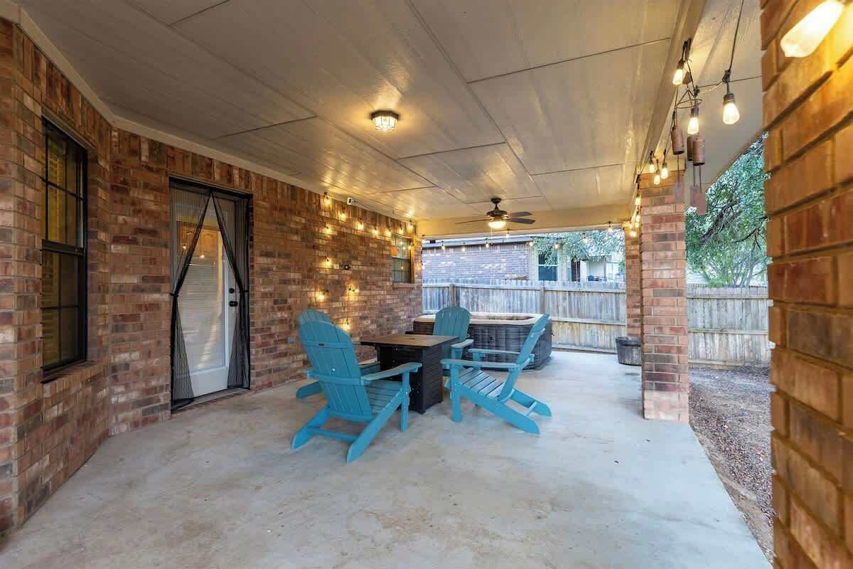 An outdoor patio with brick walls, a table, two blue Adirondack chairs, and string lights.