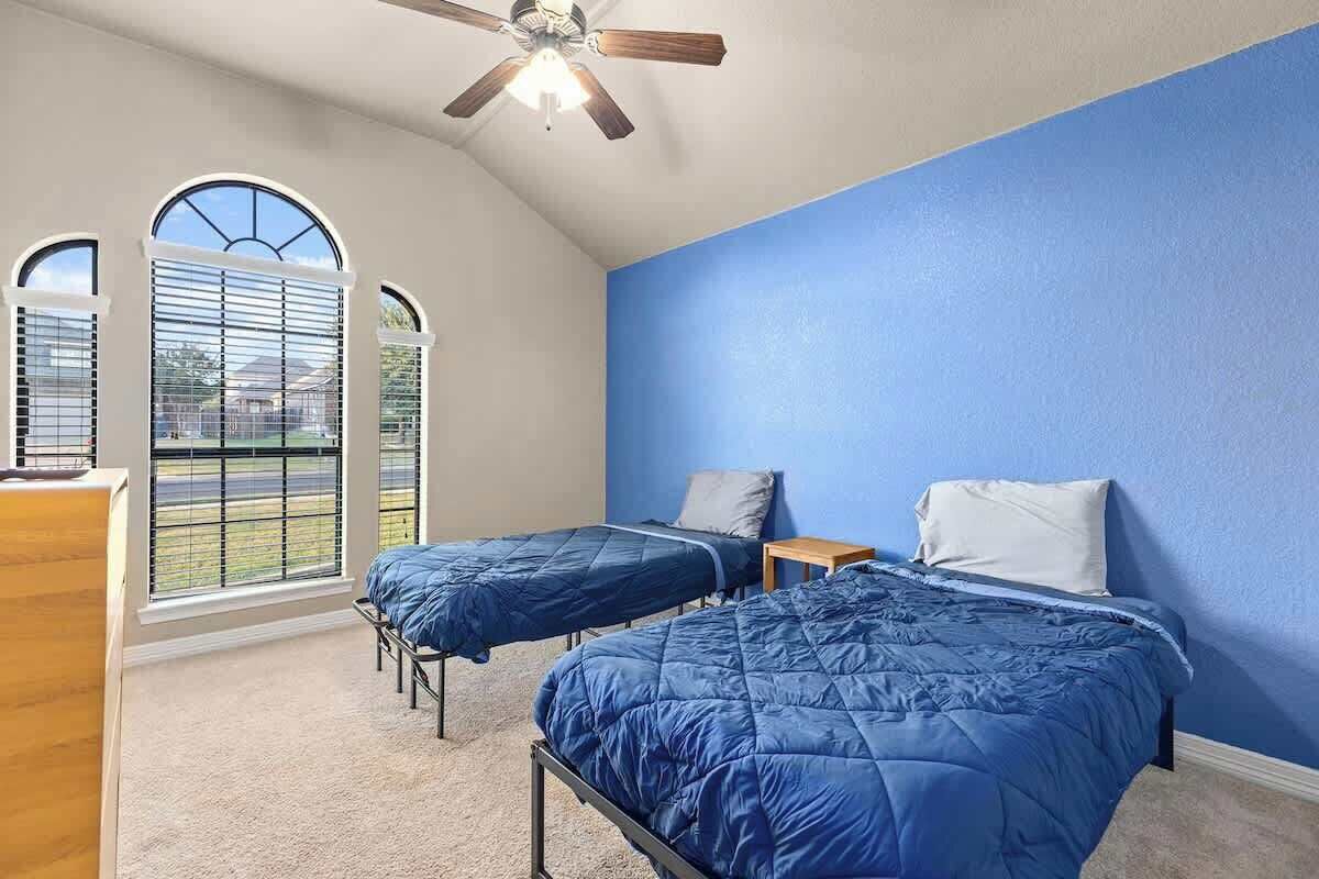 A bedroom with two beds, a ceiling fan, and large windows.