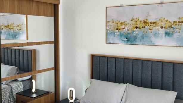 Camera da letto moderna con una testiera grigia imbottita, un comodino con specchio e un grande quadro astratto appeso al muro.
